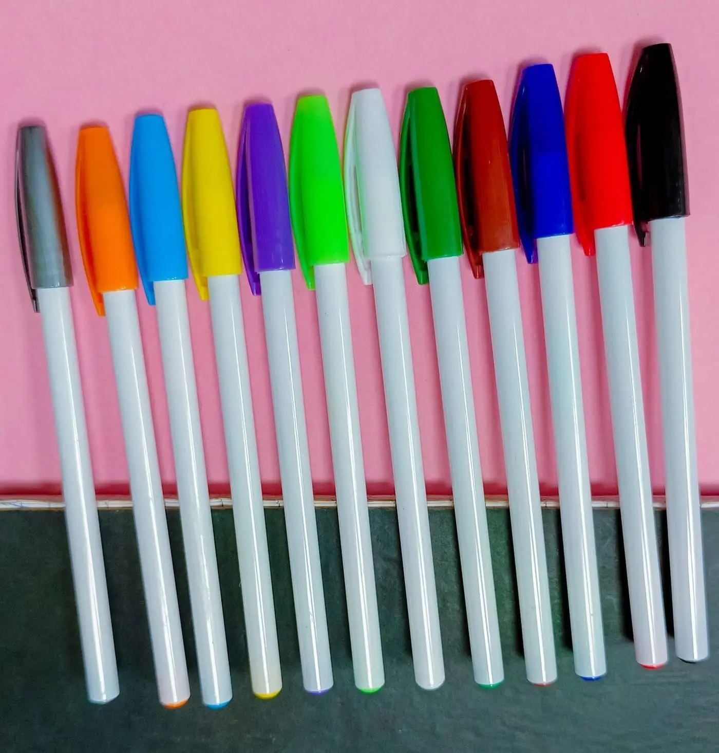White capped pens with coloured caps in a row on a pink background, Hensa
