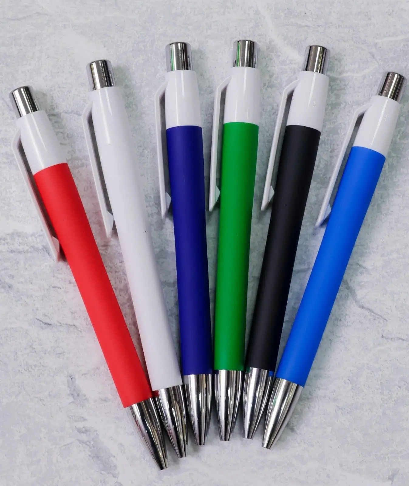 Six coloured plastic pens with chrome tops and tips on a grey surface, Hensa