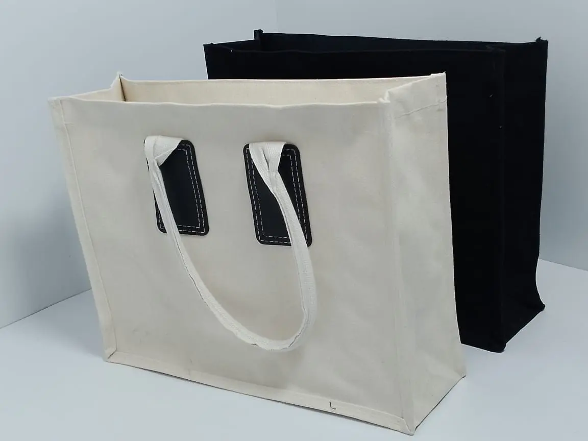 A4 cream canvas bag with a black canvas bag behind it, each with a handle and stitched patches, Hensa