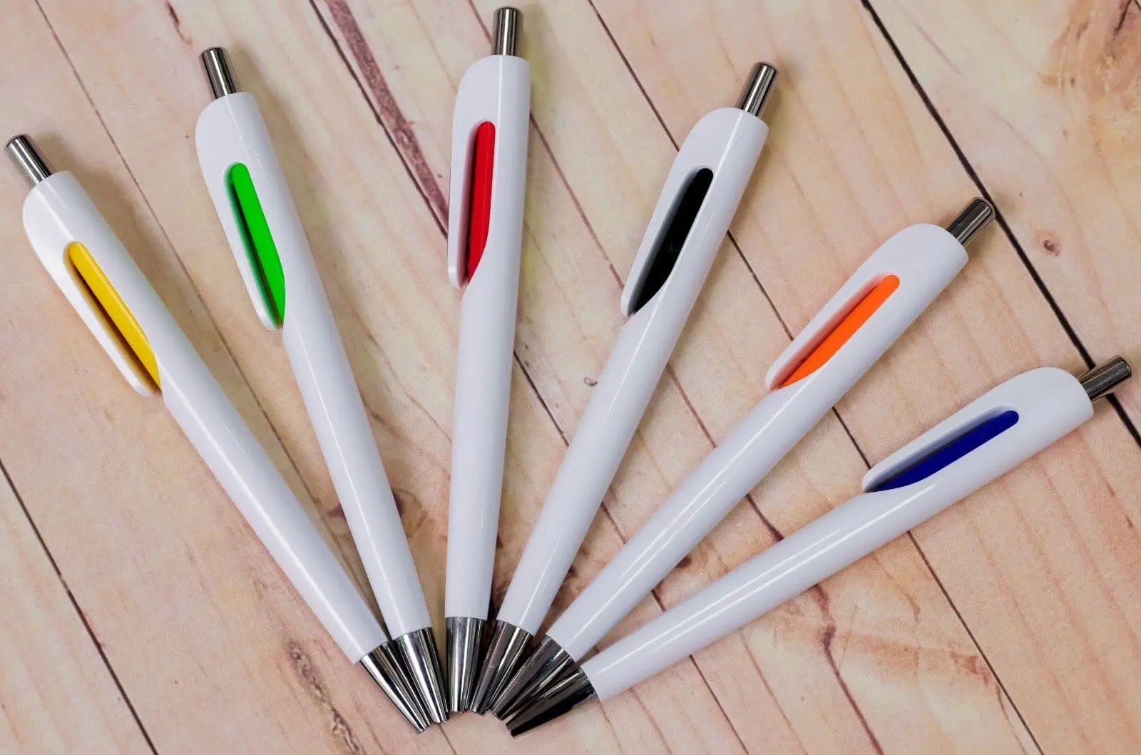 Six white pens with coloured clip inserts on a wooden floor, Hensa