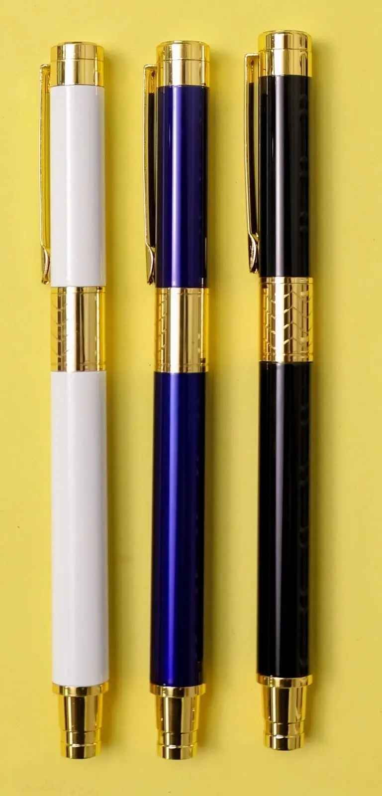 White, blue and black metal pens with gold clips and wide gold bands on a yellow surface, Hensa