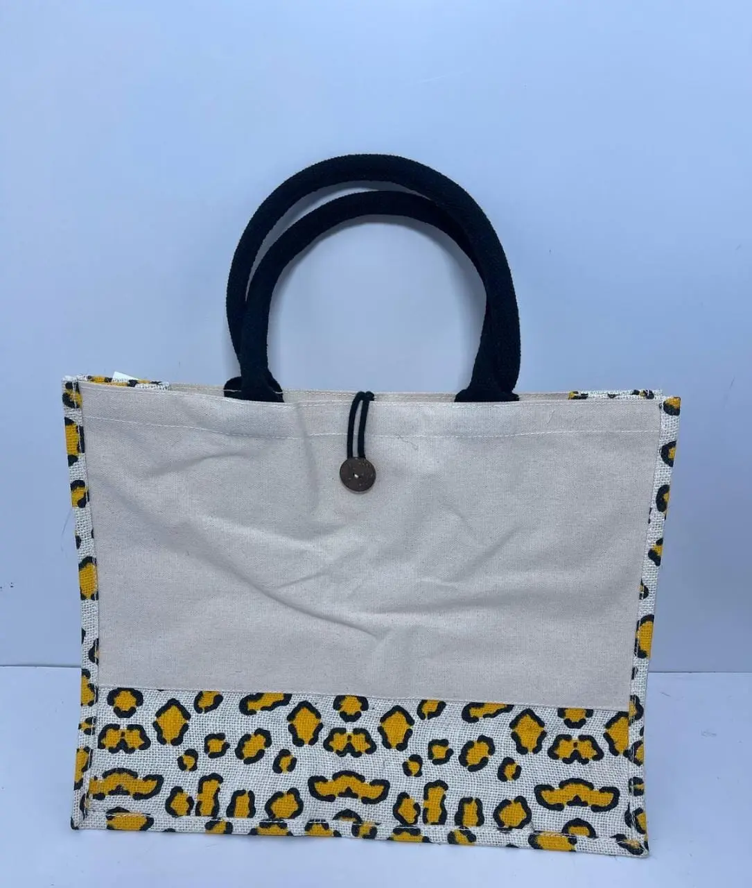 Jute bag with a yellow and black leopard-style print, a cream front panel and black handles, Hensa