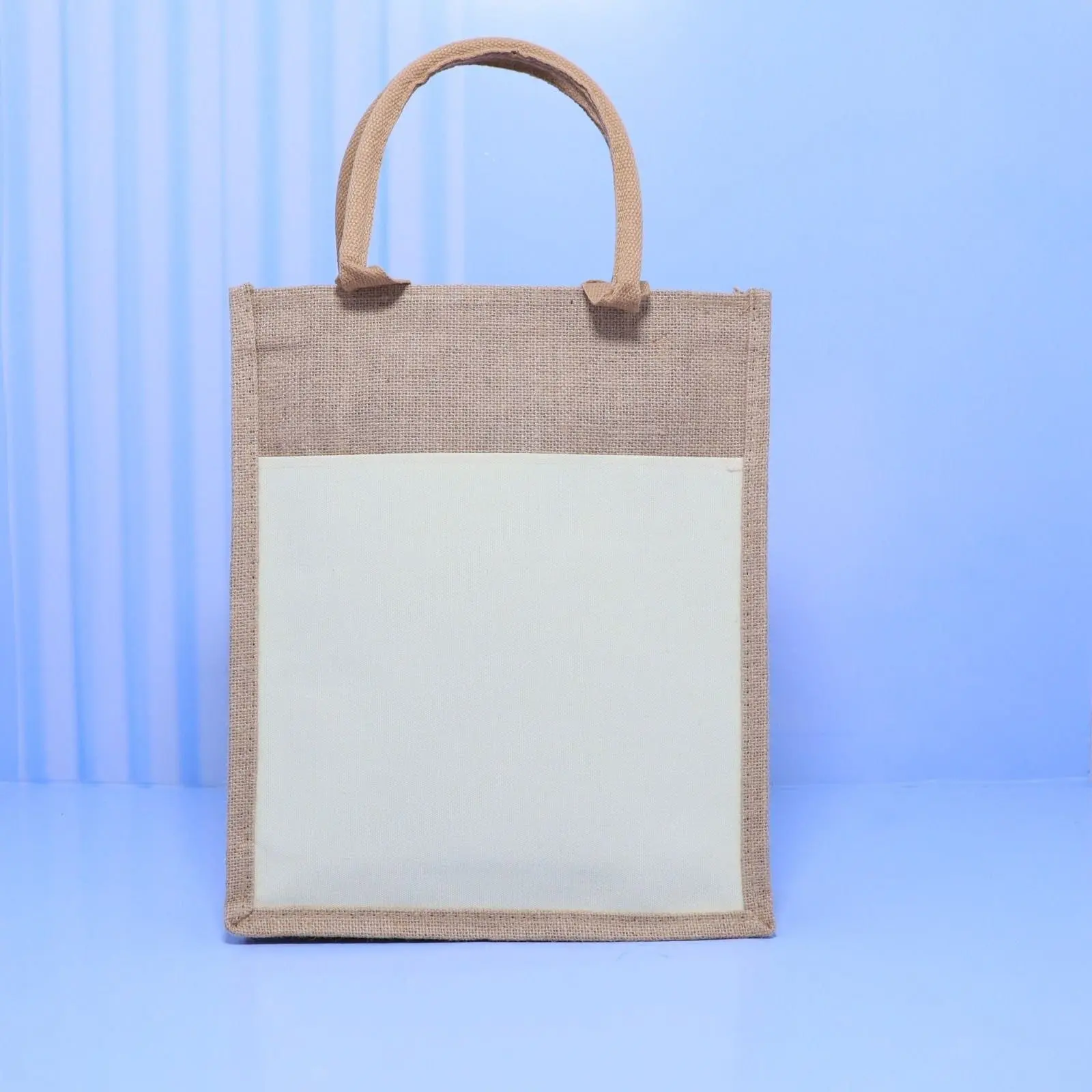 A4 natural jute bag with a cream front pocket panel and jute handles on a blue background, Hensa