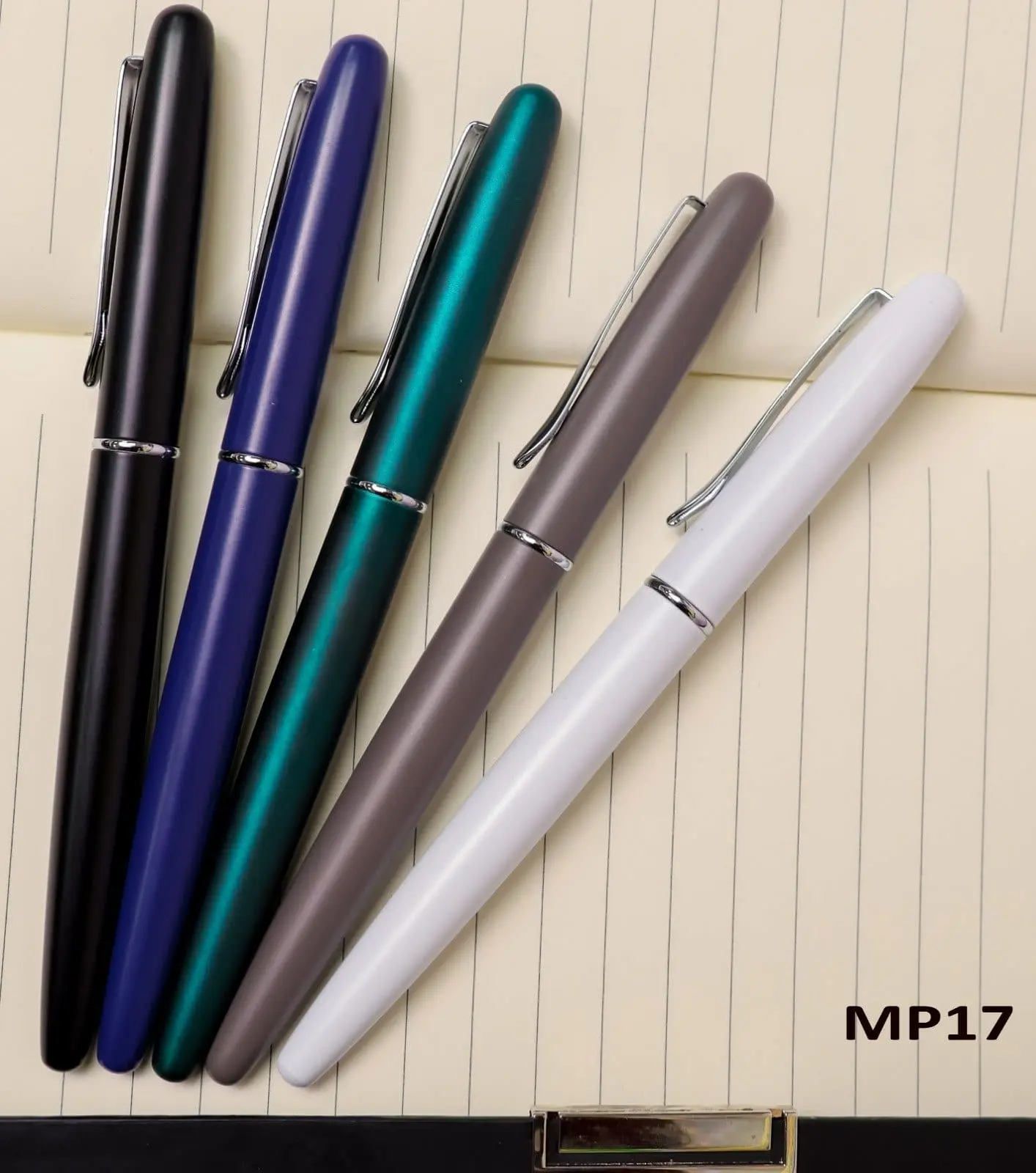 Five matte metal pens in black, blue, teal, grey and white with chrome clips on a notebook, Hensa