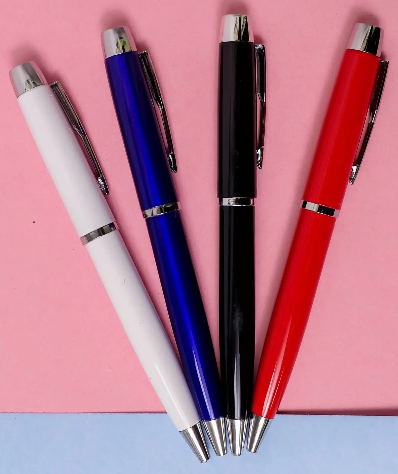 Four metal pens in white, blue, black and red with chrome caps and clips on a pink surface, Hensa