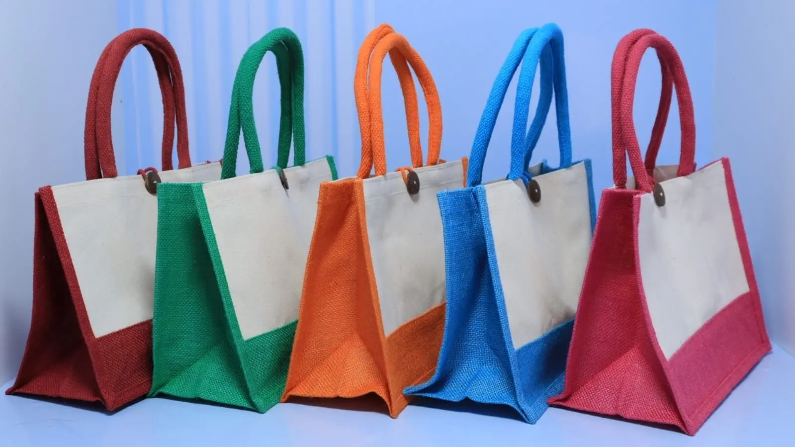 Five A5 jute bags in red, green, orange, blue and pink with cream panels and button closures, Hensa